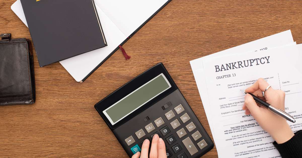 A close-up of a desk with a calculator, journal, bankruptcy law book, and bankruptcy form. Someone is filling out the form.