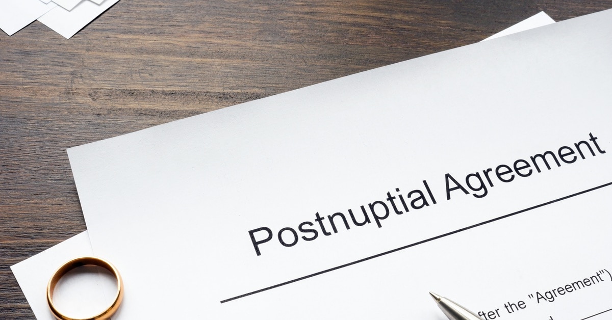 One gold ring and a silver pen sitting on top of a document with the title heading "postnuptial agreement."