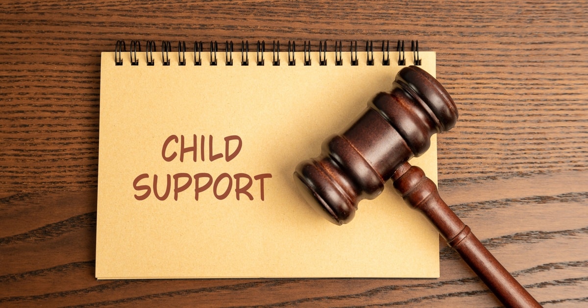 A brown gavel rests on a notepad with the words "child support" written on it. The gavel and notepad sit on a wooden surface.