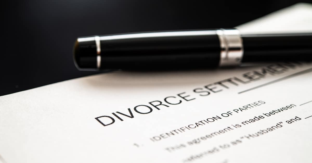 A black pen on top of a document with the title heading "divorce settlement." The document rests against a black surface.