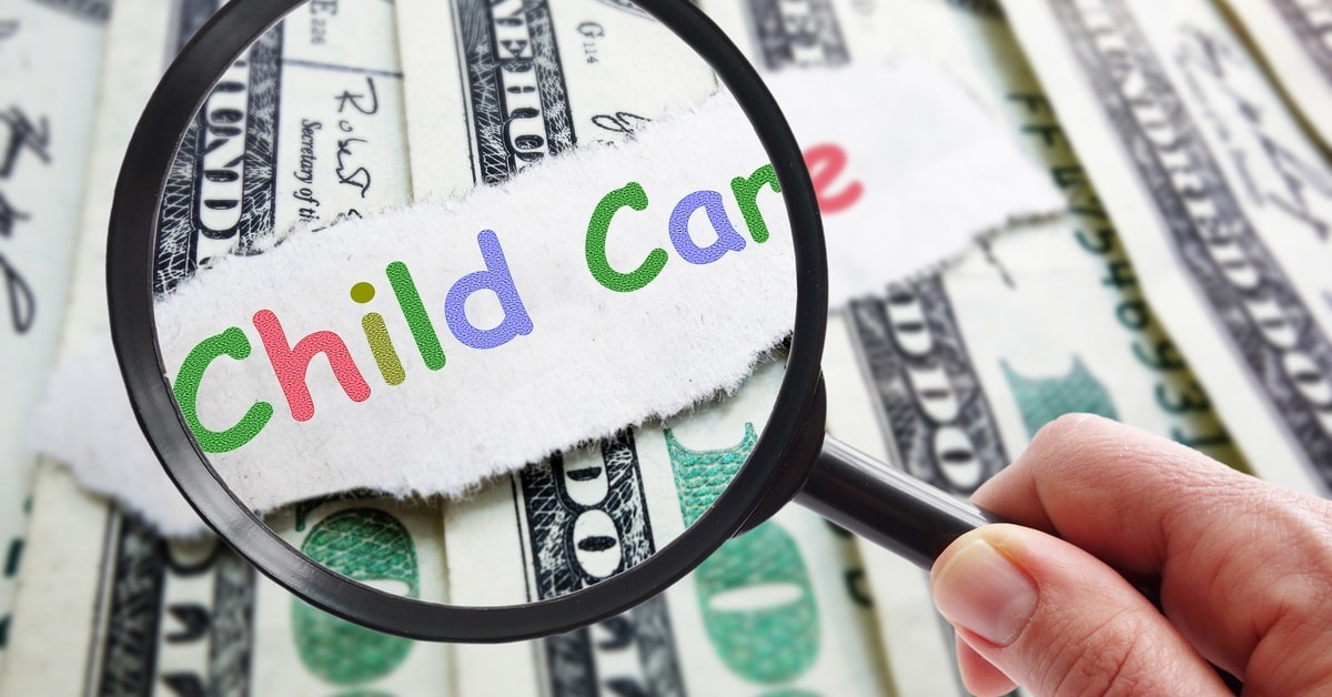 A magnifying glass held to a paper slip with the words "child care" written on it in colorful letters on top of paper money.