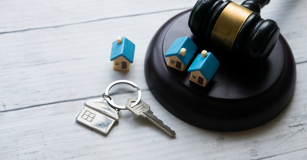 A judge's gavel and two mini model homes rest on the sound block. To the side is another model home and some silver house keys.