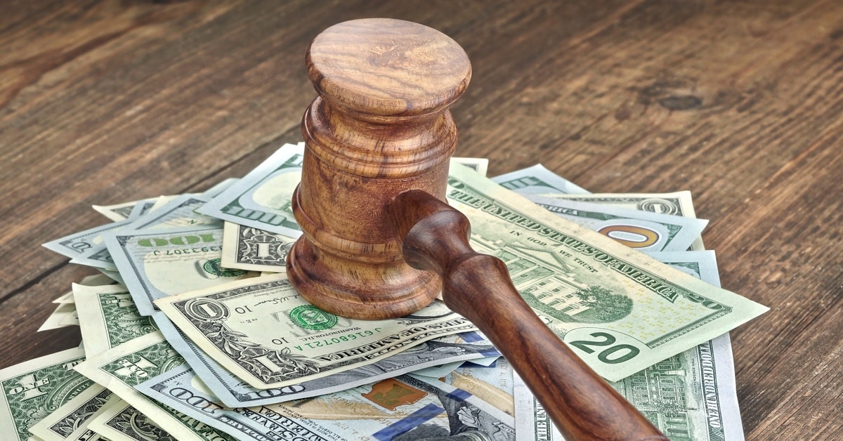 A judge's wooden gavel sitting on top of a pile of US currency, including 1-dollar, 20-dollar, and 100-dollar bills.