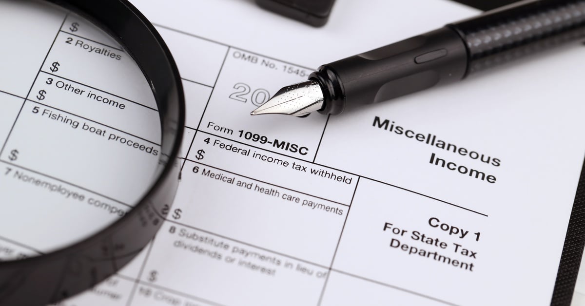 A close-up of a blank1099 Miscellaneous Income form underneath a magnifying glass and a calligraphy pen.