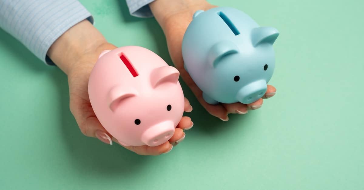 A person holding two piggy banks, one pink and one blue, in both hands against a mint green background.