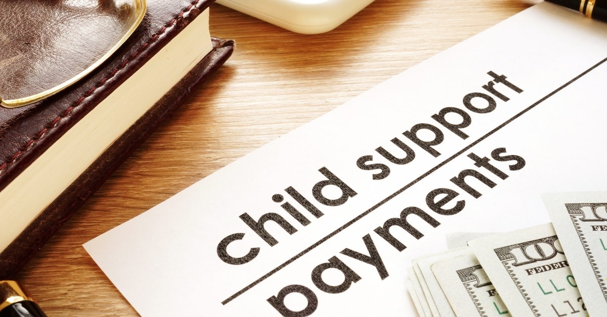 A document titled "child support payments" surrounded by cash, a pen, a notebook, glasses, and a calculator.